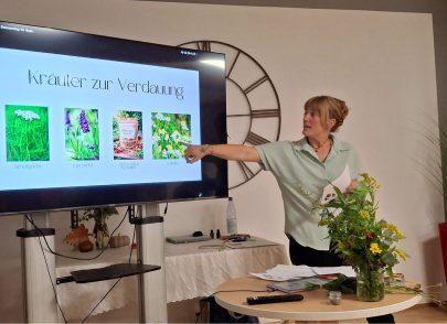 Frau Gottstein zeigt auf eine Vortragsfolie "Kräuter bei Verdauung"
